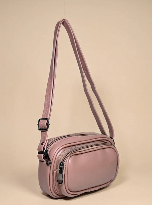 Mauve crossbody handbag with double zippers and adjustable strap on beige background