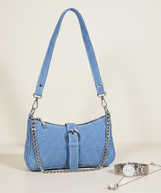 Light blue denim shoulder bag with silver chain strap, displayed beside a silver watch and necklace on a beige surface.