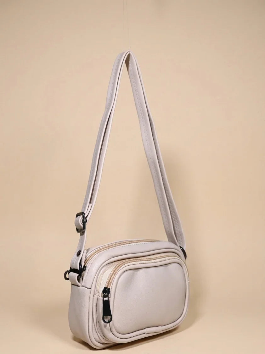 Beige crossbody handbag with front zip pocket and adjustable strap on neutral background