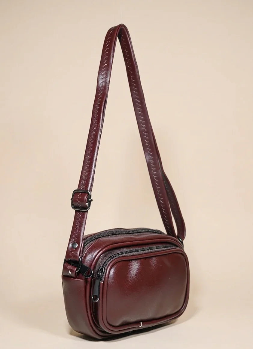 Brown leather crossbody handbag with adjustable strap and front zipper pocket on beige background