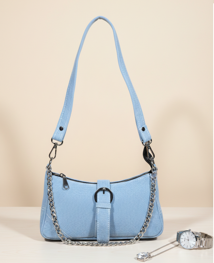 Light blue shoulder bag with silver chain strap, displayed on a table next to a watch and necklace.