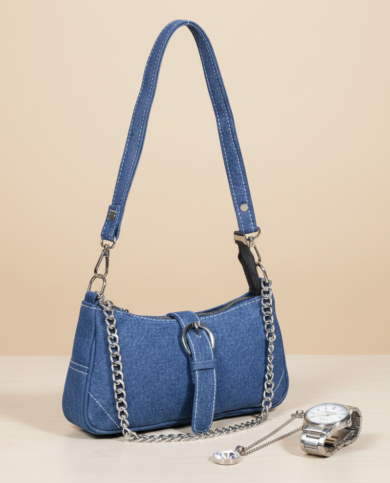 Blue denim shoulder handbag with silver chain strap, displayed on a wooden surface next to a silver watch and pendant.