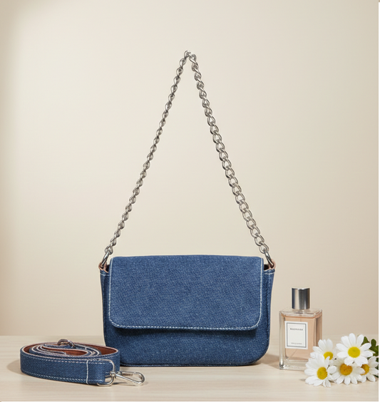Blue denim handbag with chain strap, detachable shoulder strap, perfume and daisies on table