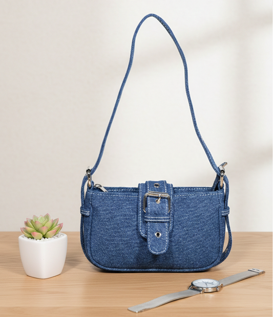 Blue denim handbag with buckle detail on a wooden table, next to a succulent and wristwatch