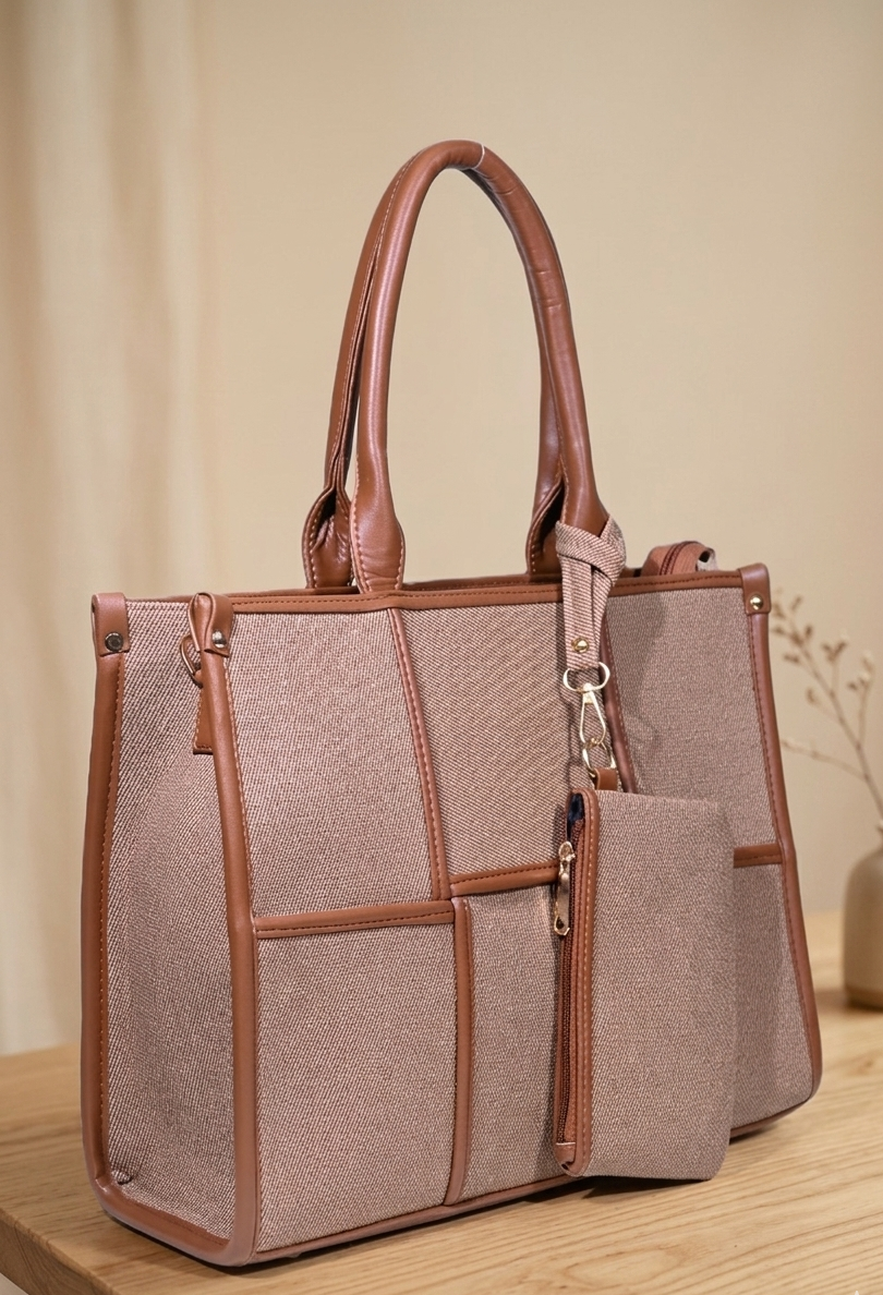Taupe structured handbag with brown leather trim and detachable pouch on wooden table